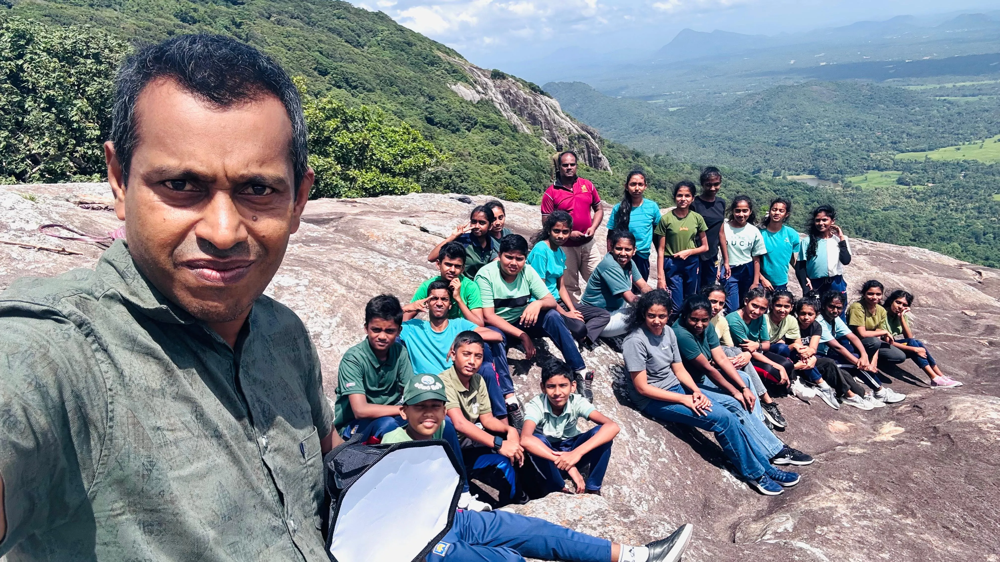 Nayana Pradeep taking a selfie with the group on the Dolukanda summit, valley behind.