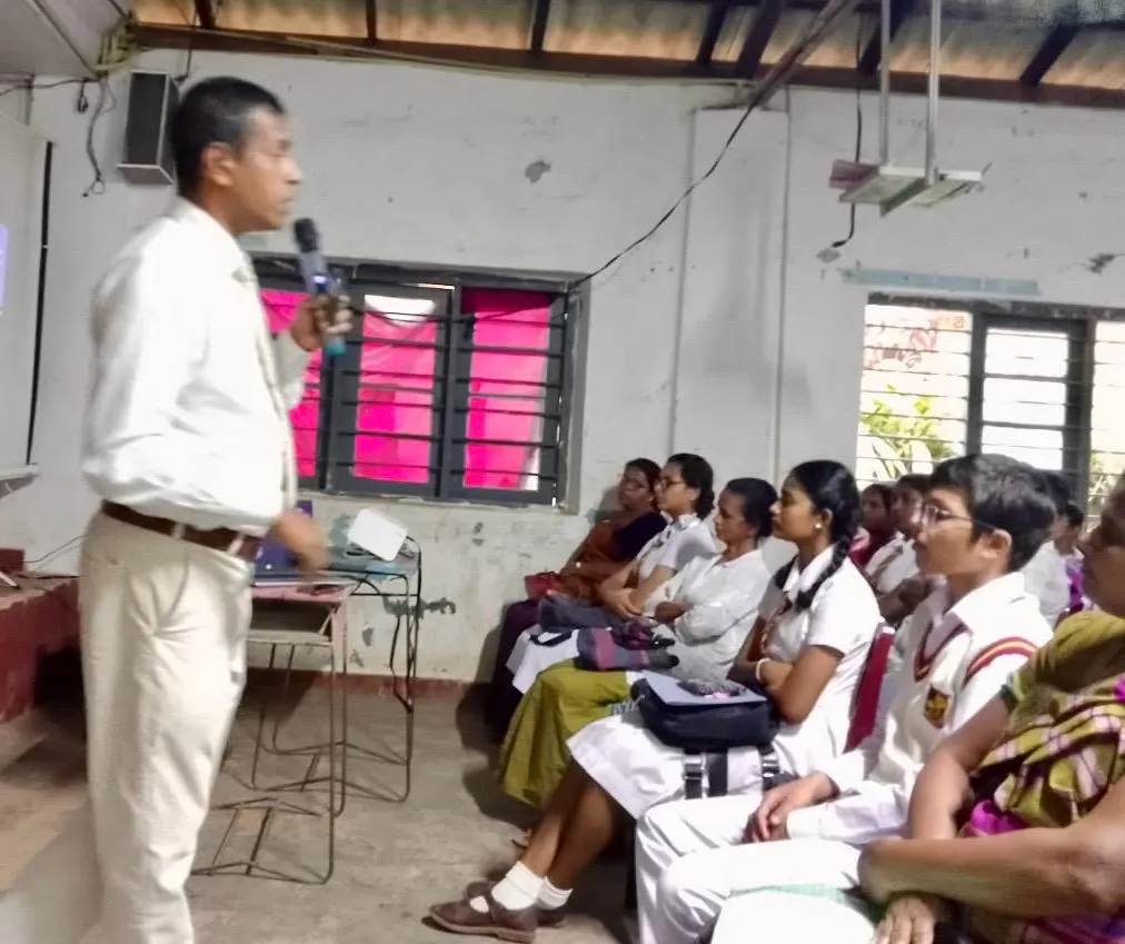 Nayana Pradeep addressing students and parents seated along the side of the hall.