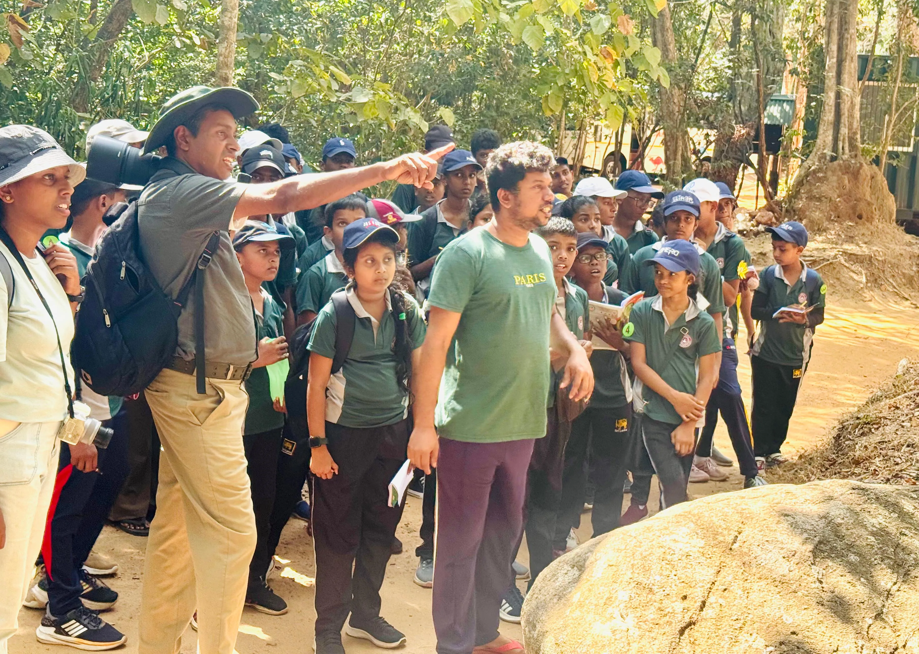 Nayana Pradeep pointing something out to students beside a boulder in the forest.