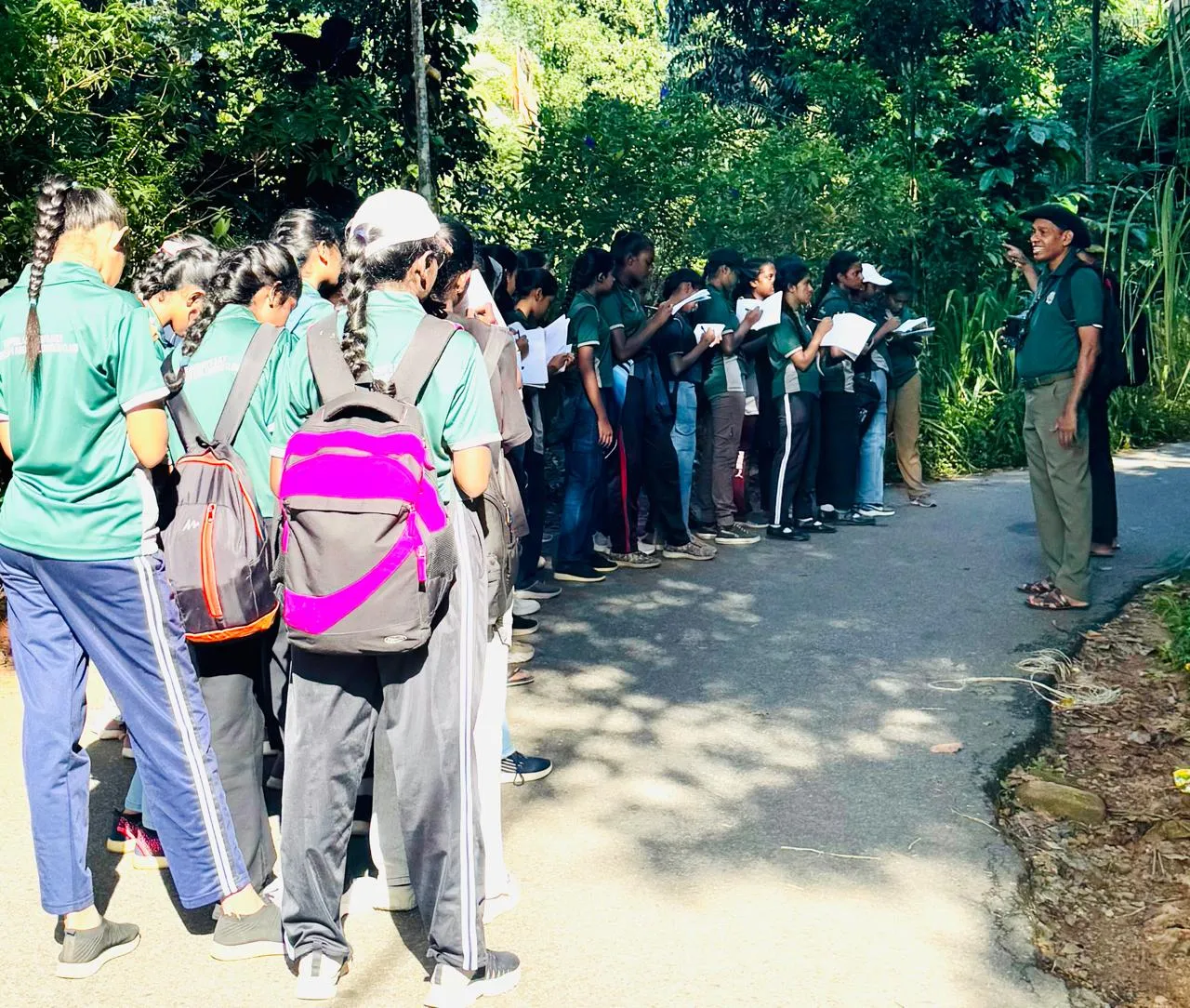 Nayana Pradeep explaining to a line of students taking notes on a forest path.
