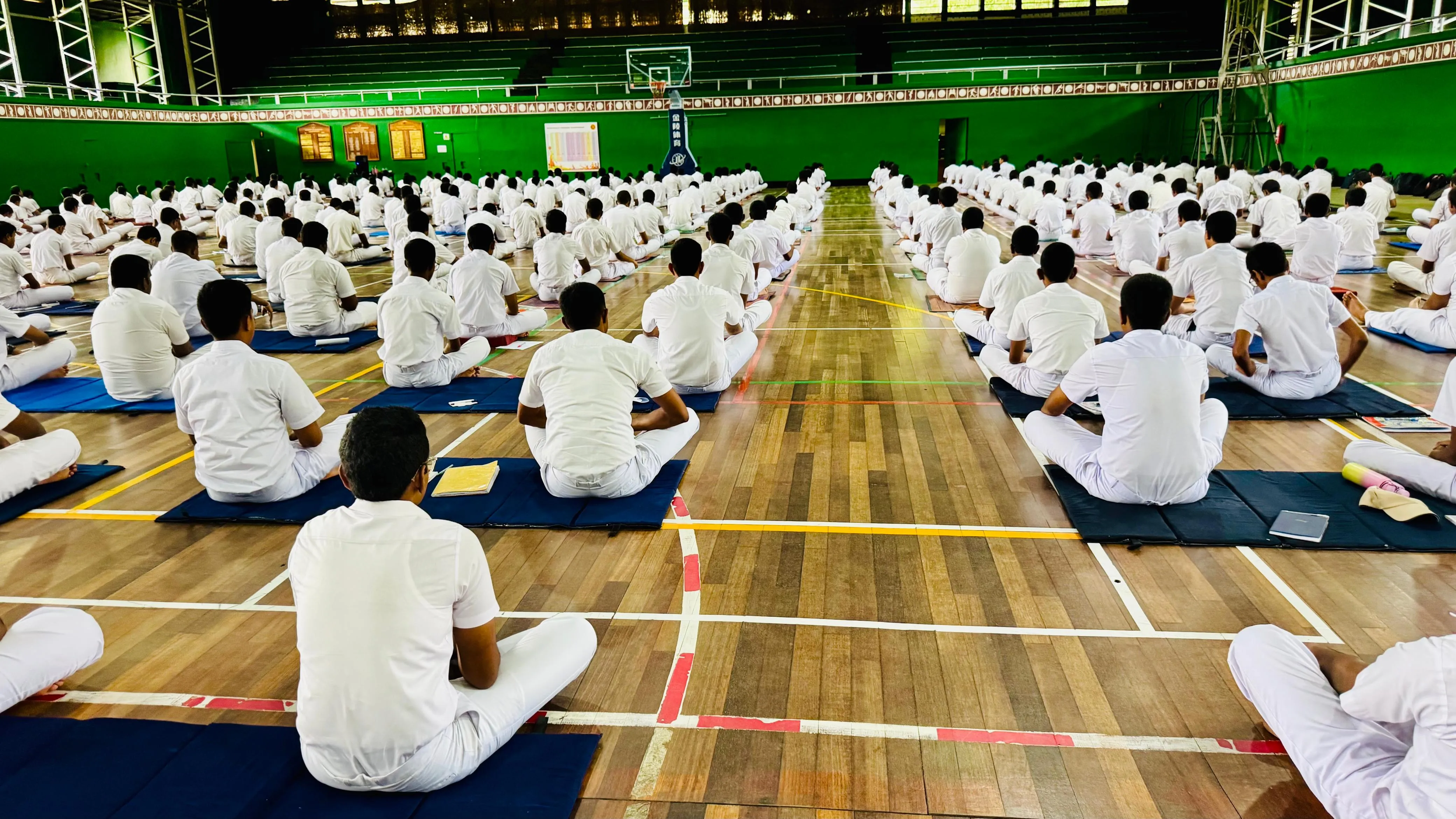 Students in white uniforms seated cross-legged on mats, meditating.