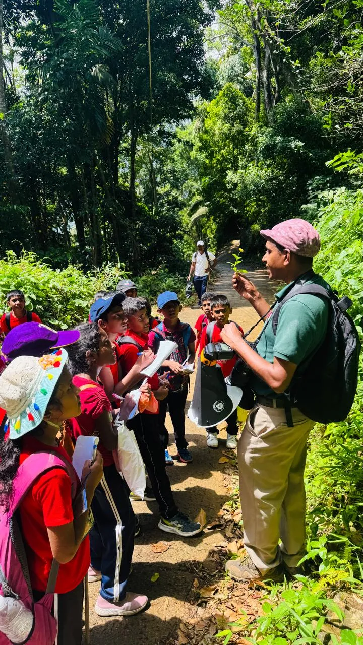Nayana Pradeep showing a leaf to attentive students on a forest path.