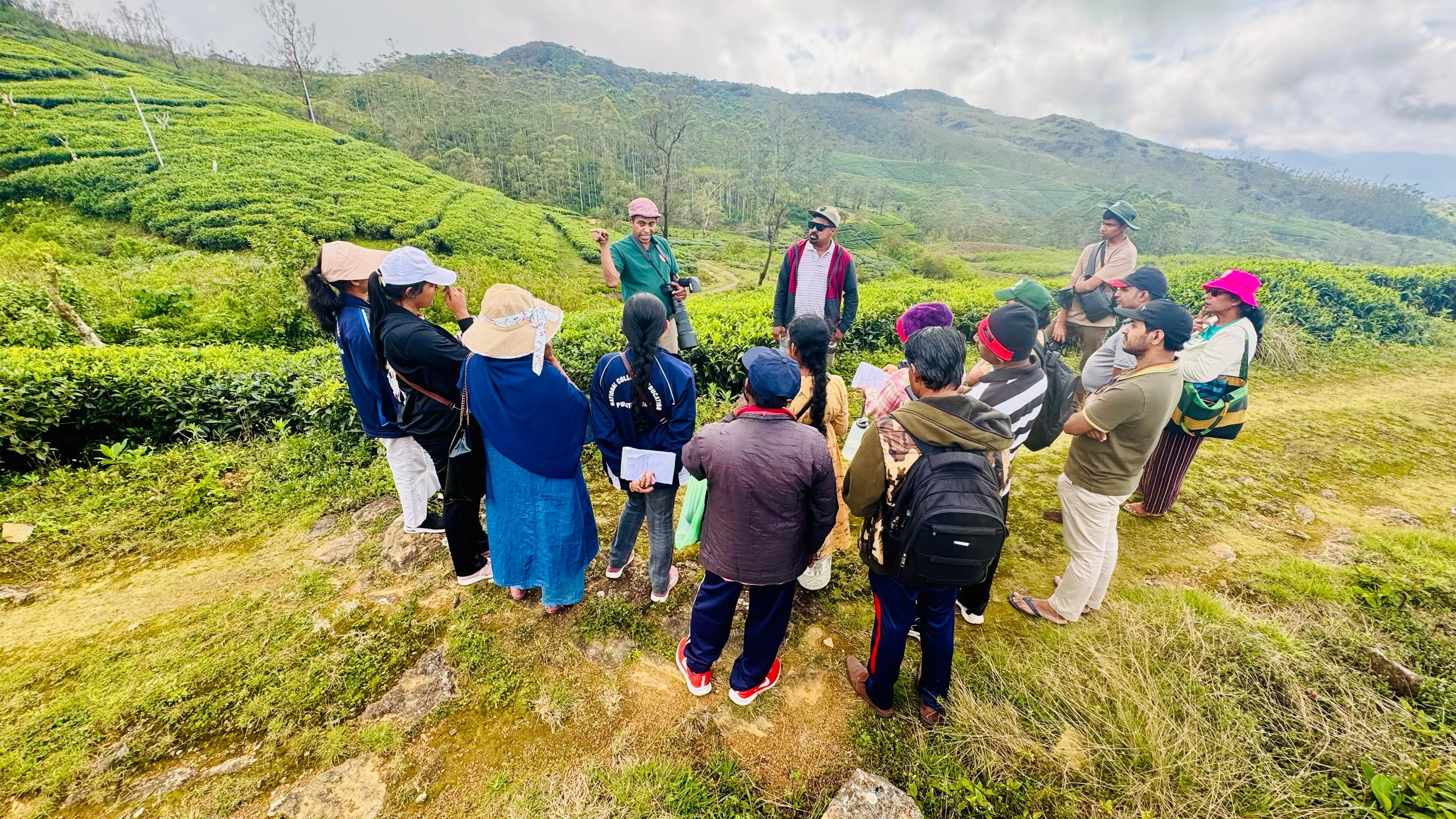 The group gathered around Nayana Pradeep for a field talk, with mountains behind.