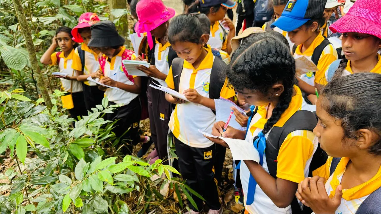 Students in yellow-and-white uniforms taking field notes while observing forest plants.