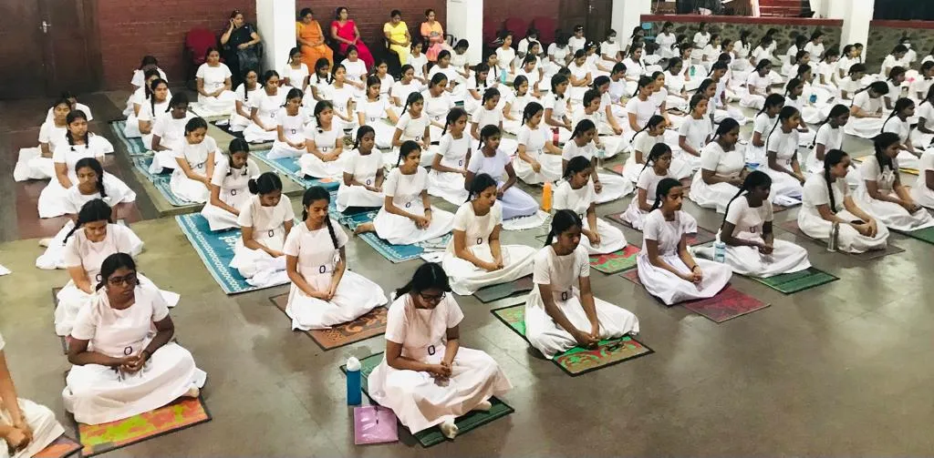 A large group of students practising seated meditation in the school hall.