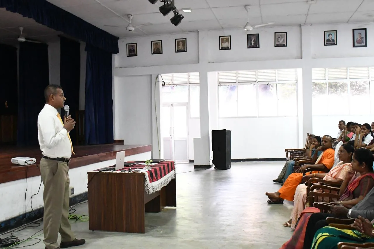 Nayana Daundasekara addressing A/L students and parents in the Kegalu Balika Vidyalaya hall, with guests seated in the front row.